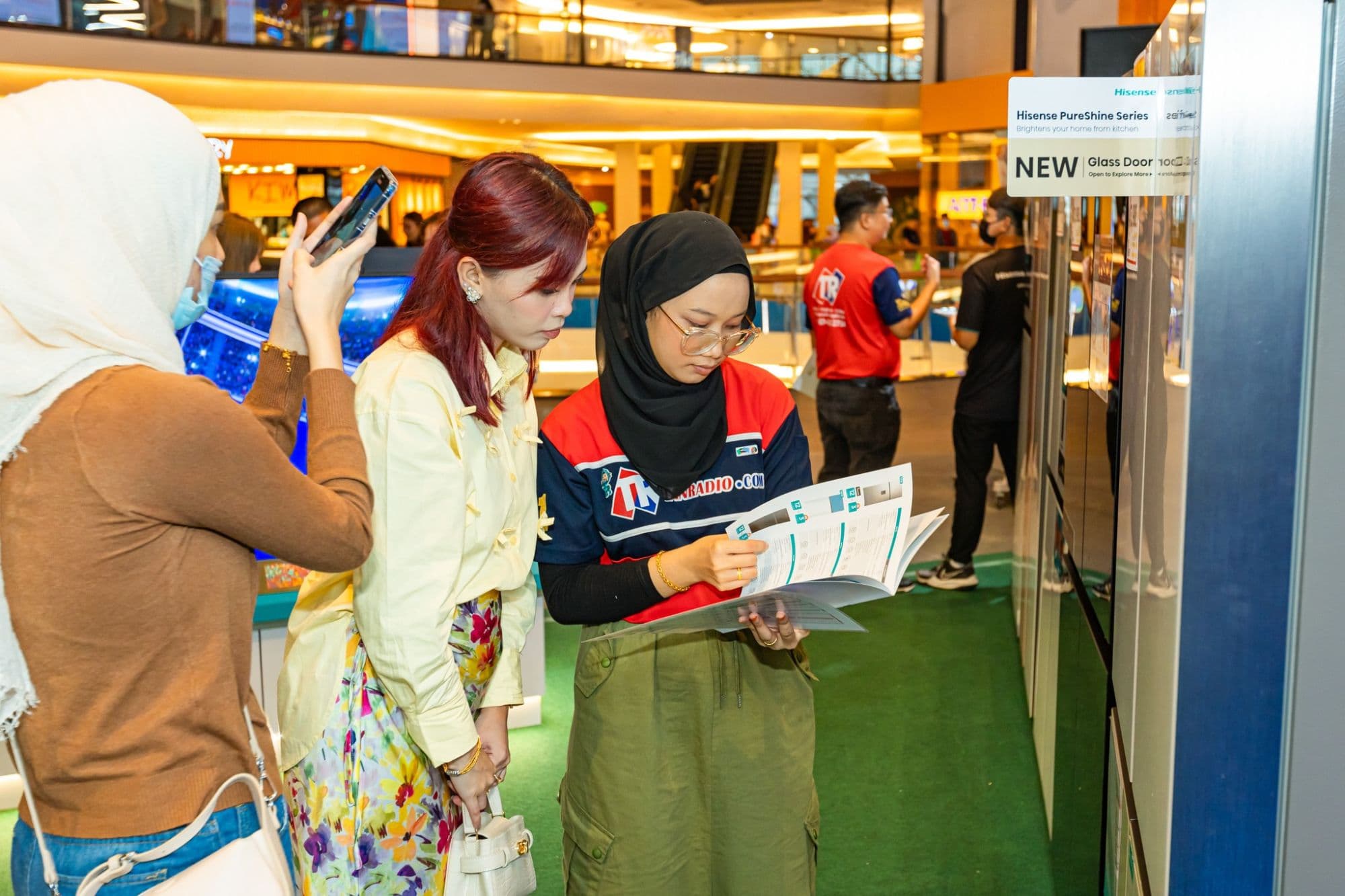 A Tanradio sales associate walks two customers through a Hisense PureShine product brochure at a branch.